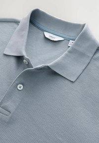 Ljusgrå polo skjorta med en strukturerad tyg, en kontrasterande krage och två knappar. En tagg märkt "NEXT" synlig inuti kragen.