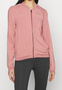 Bomber jacket rosa chiaro con chiusura a zip frontale, polsini e fondo a costine, e tasche laterali, realizzato in tessuto morbido e liscio.