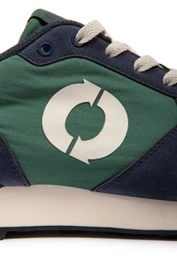 Vue latérale d'une basket verte et bleu marine avec un symbole de recyclage blanc circulaire et des lacets beiges sur une semelle blanche.
