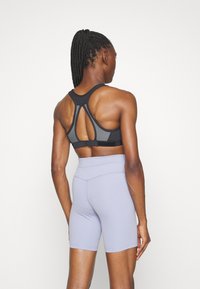 Black sports bra with a racerback design and mesh accents, paired with light purple high-waisted shorts, showcasing smooth fabric textures.