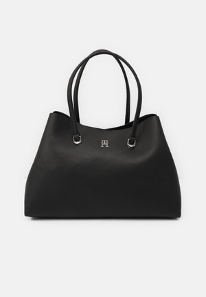 Schwarze Leder-Tote-Bag mit strukturierter Oberfläche, ausgestattet mit zwei Griffen und einem silbernen Logo-Element auf der Vorderseite. Minimalistisches Design.