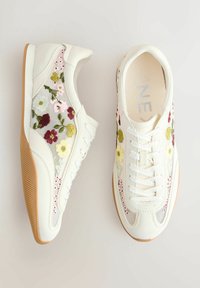 Baskets blanches avec semelles en caoutchouc, ornées de broderies florales multicolores sur des panneaux en mesh, vues de dessus avec les lacets attachés.