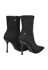 Botines negros hasta el tobillo de tela suave, con punta afilada, tacón alto de aguja y cierre con cremallera lateral. Detalle sutil del logo metálico en el tacón.