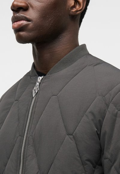 Chaqueta bomber acolchada gris con cuello de canalé y cierre de cremallera plateada, que presenta una tela elegante y texturizada con un patrón de rombos.