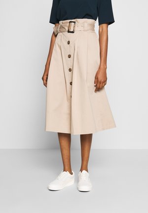 Falda midi de algodón beige con cintura con cinturón, botones delanteros y diseño fluido, combinada con zapatillas blancas.