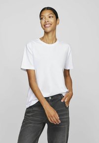 Hvit crew neck t-skjorte laget av bomull, med korte ermer og en avslappet passform, parret med mørkegrå denimbukser.