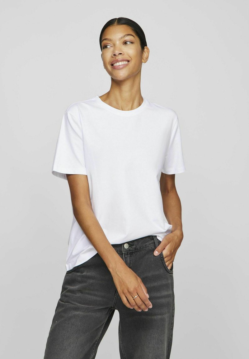 Hvit crew neck t-skjorte laget av bomull, med korte ermer og en avslappet passform, parret med mørkegrå denimbukser.