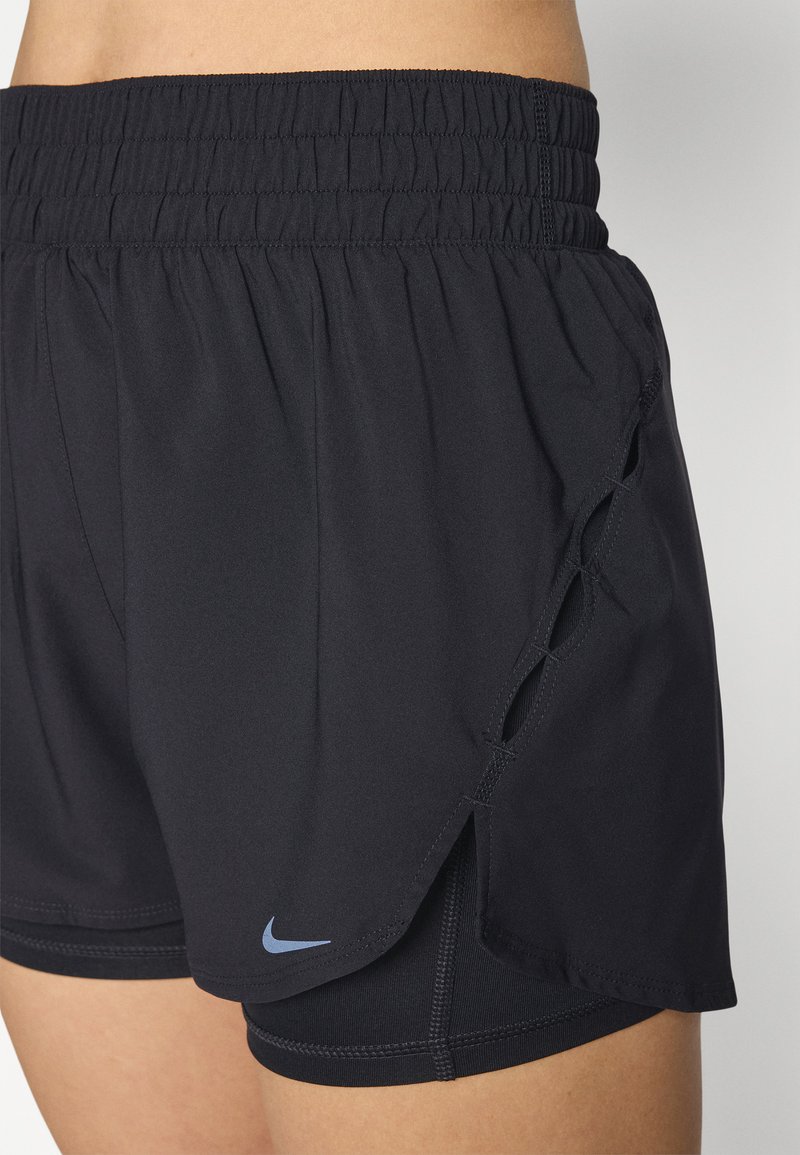 Pantalones cortos deportivos negros con una amplia cintura elástica, detalles recortados en los laterales y un pequeño logo azul de Nike en el dobladillo. Textura de tela suave.