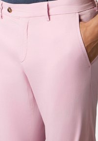 Pantaloni rosa chiaro caratterizzati da una texture liscia, tasche laterali e una chiusura con bottone in vita, progettati per una vestibilità su misura.