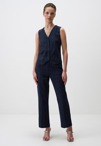 Navy gestreepte vest en bijpassende broek van textuurstof. Het vest heeft knopen aan de voorkant; de broek is op maat gemaakt met een rechte pijp.