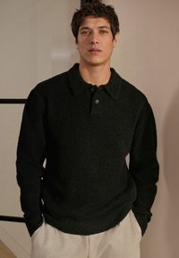 Sort, tekstureret langærmet polo med krave og tre knapper. Båret med lysegrå sweatpants.
