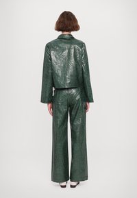 Dwuczęściowy, zielony, teksturowany strój wykonany z błyszczącego materiału. Krótka kurtka ma kołnierz, a spodnie o szerokich nogawkach mają luźny krój.