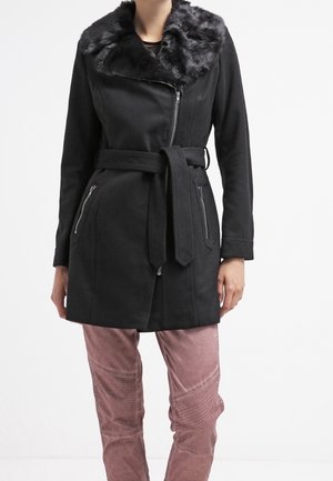 Abrigo negro con cuello de piel sintética, cierre frontal con cremallera y bolsillos laterales. Cuenta con un cinturón ajustable y una tela texturizada. Combinado con pantalones rosas.