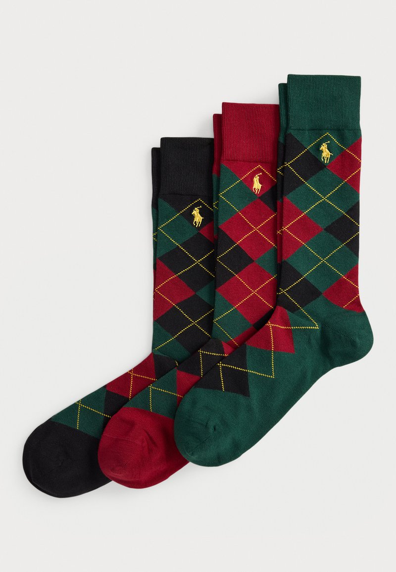 Tres pares de calcetines argyle doblados en negro, rojo y verde oscuro, con costuras amarillas y un pequeño logo bordado en oro en cada puño.