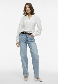 Hvid langærmet bluse med V-hals og samlede manchetter, parret med lyseblå lige ben jeans og beige spidse hæle.