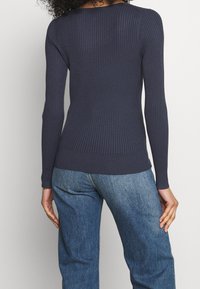 Marinblå långärmad ribbad topp med rund halsringning, figurnära passform och texturerad tyg. Kombinerad med ljusblå, avslappnade jeans.