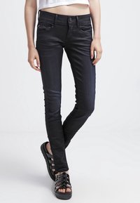 Svarta slim-fit jeans med en jämn textur, diskreta framfickor och en funktionell midja med en knapp. Bärs med svarta sandaler.