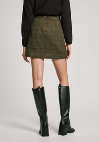 Green plaid mini skirt with a fitted waist and subtle texture, paired with knee-high black boots featuring a rectangular block heel.
