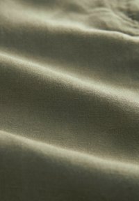 Tejido en verde oliva que muestra una textura suave, con pliegues suaves y un brillo sutil. El material parece ligero y finamente tejido.
