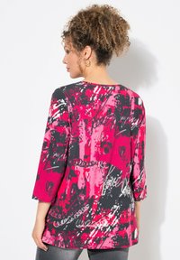 Multikleurige top met een abstract patroon in roze, zwart en wit, driekwartmouwen en een ronde halslijn. Gladde stof textuur.