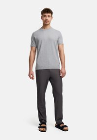 Camiseta gris de manga corta, con dobladillo acanalado, combinada con pantalones de rayas oscuros y sandalias negras con correas ajustables.
