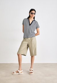 Stripet kortermet topp med V-hals og marineblå detaljer, sammen med khaki knelengde shorts og lyse sandaler med tykke såler.