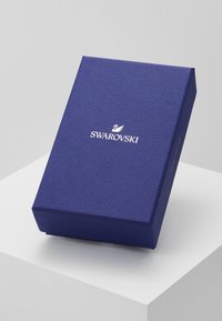 Scatola regalo Swarovski, forma rettangolare, materiale blu scuro testurizzato, logo in rilievo bianco sulla parte superiore, bordi puliti, presentata in prospettiva.