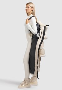 Gewatteerde jas met een zwart-crèmekleurig ontwerp, voorzien van een met bont gevoerde capuchon, ritssluiting en drukknoopsluitingen, en twee zijzakken. Zachte textuur.