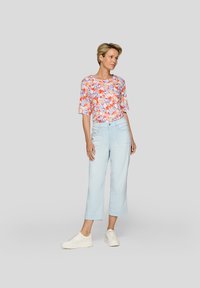 Floral-patterned short-sleeve top with a round neckline in orange and pink tones, paired with light blue cropped pants and white sneakers.