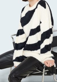 Czarnobiały sweter w paski wykonany z miękkiej, teksturowanej tkaniny; posiada okrągły dekolt i szerokie rękawy. Połączony z czarnymi skórzanymi spodniami.