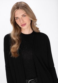 Cardigan leggero nero con vestibilità ampia, design aperto davanti, indossato su una maglietta nera. Texture liscia e semplicità monocolore.