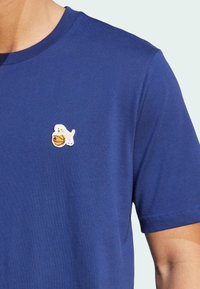 Blå kortærmet t-shirt i blødt stof med et hvidt broderet segl og basketball-design på venstre brystområde.