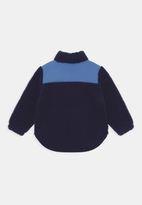 Navy blue fleece jacket with light blue nylon panel on upper back, long sleeves, and high collar, shown from the back.