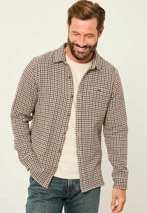 Braun- und cremefarbenes Hahnentrittmuster-Hemd mit Knopfverschluss, langen Ärmeln und lockerer Passform, über einem hellbeigen T-Shirt getragen.
