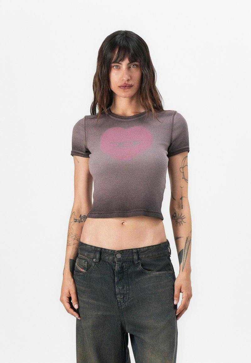 Gray cropped t-shirt with short sleeves featuring a faded pink heart graphic. Paired with dark, loose-fitting denim jeans.