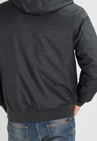 Mörkgrå hoodie med en texturerad yta, en huva och ribbade ärmslut och nederkant. Matchad med ljusblå jeans för en avslappnad look.