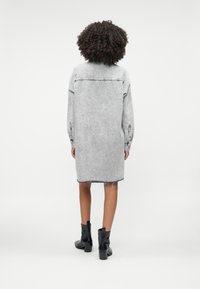 Szara sukienka dżinsowa z długimi rękawami, surowym dołem i zapinanymi mankietami. Połączona z czarnymi botkami na obcasie dla kontrastu.