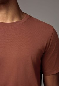 Tricou maro cu guler rotund și mâneci scurte, realizat dintr-un material moale, având o textură netedă și un design simplu.