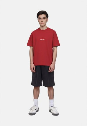 Red crew-neck t-shirt with short sleeves and white text. Paired with black shorts, white socks, and gray sneakers with black accents.