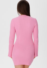 Robe en maille côtelée rose vif, coupe moulante, manches longues, encolure ronde, et longueur mi-cuisse. Texture lisse.