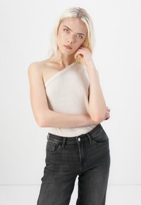 Beige ribbed one-shoulder top paired with high-waisted dark gray jeans. The outfit features a fitted design with textured fabric.