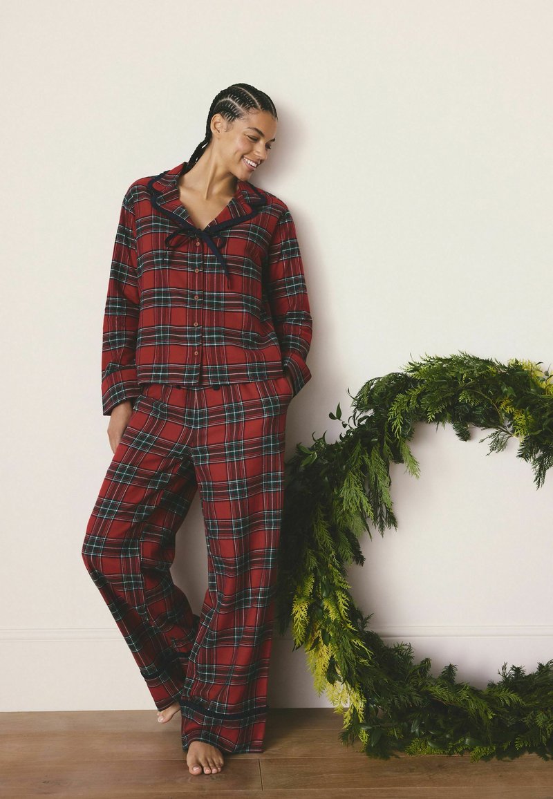 Rød ternet flannel pyjamas sæt med lange ærmer og brede bukser, med krave og knaplukning foran. Kombineret med en grøn foliede accent.
