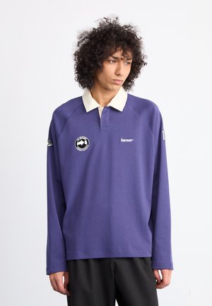 Polo a maniche lunghe viola con colletto color crema, dotato di toppe con logo sul petto e sulla manica, realizzato in un tessuto liscio.