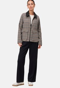 Veste à motif pied-de-poule avec un col noir, dotée de deux poches avant et d'une coupe décontractée. Associée à un pantalon large noir et des baskets blanches.