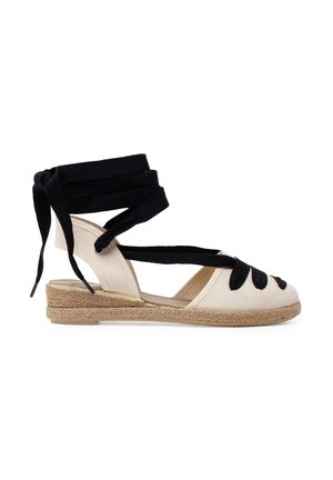 Alpargata de cuña color crema con cordones de tela negra. Presenta una suela envuelta en yute y un diseño recortado en la puntera. Tacón plano.