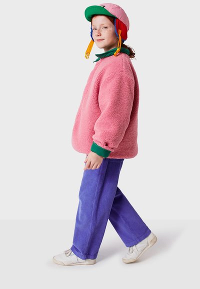 Rosa fleece-pullover med grön krage, parat med lösa lila corduroybyxor och vita sneakers. Färggad mössa med öronlappar.