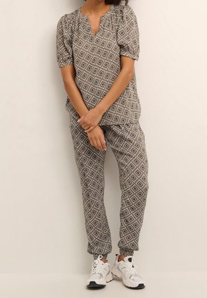Ensemble deux pièces comprenant un haut à motifs géométriques avec des manches bouffantes et un pantalon fuselé assorti, le tout dans des nuances de marron et de crème.