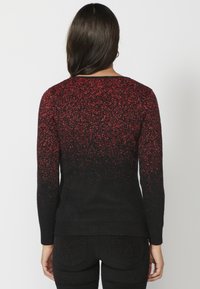 Strickpullover mit schwarzem Grundton, der einen rot gesprenkelten Farbverlauf aufweist. Lange Ärmel, runder Ausschnitt und geripptem Saum. Glatte Textur.