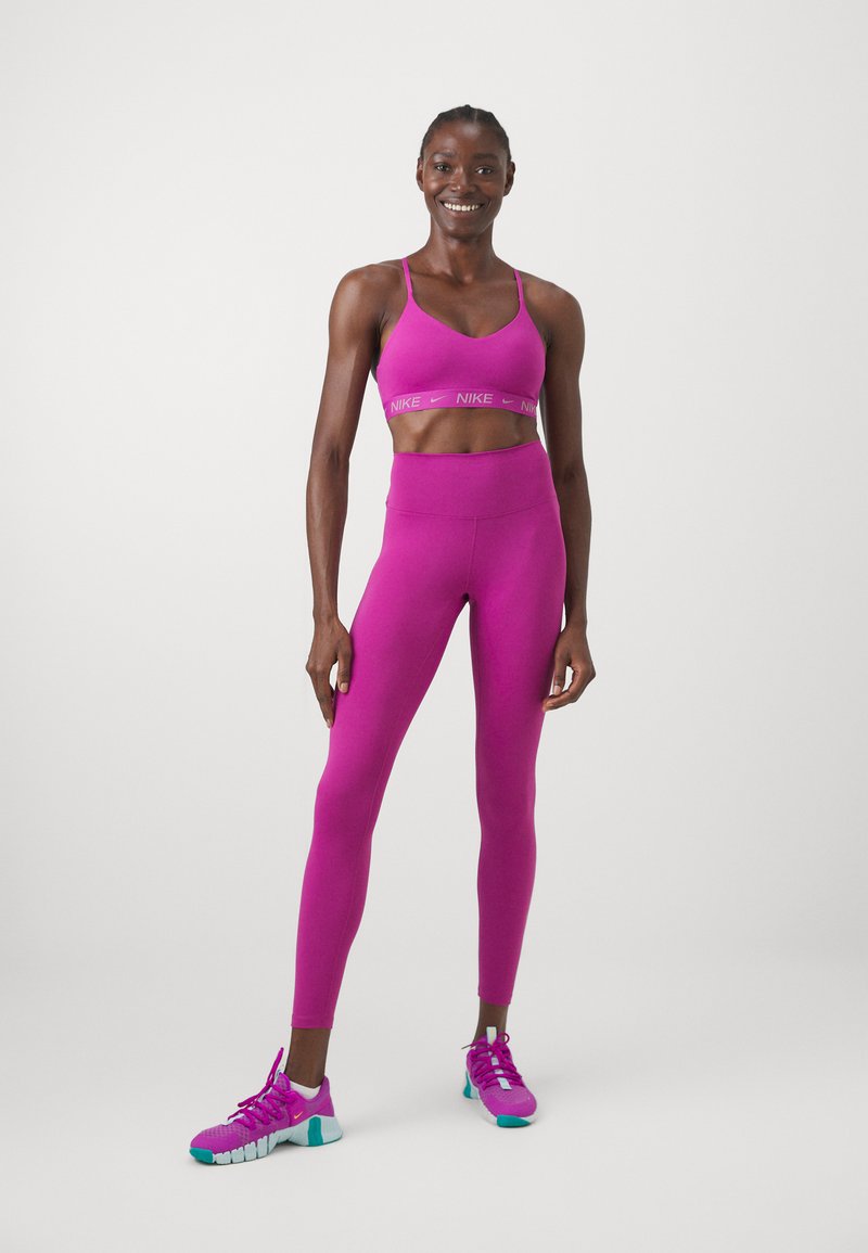 Sostén deportivo fucsia con el logotipo de Nike, leggings de cintura alta fucsias a juego y zapatillas deportivas moradas con acentos en teal. Textura suave.