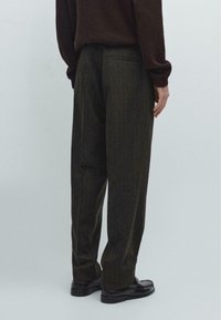 Maglione lavorato a maglia marrone abbinato a pantaloni grigi scuri, texturizzati con sottili righe. Vestibilità ampia, con tasca posteriore e scarpe flat.